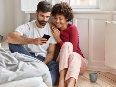 Couple in love watch interesting video on cell phone, enjoy togetherness, high speed internet connection, rest at cozy apartment interior, have free time and day off. Technology and lifestyle concept