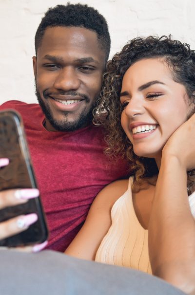 Young couple using a mobile phone while sitting on couch at home. Stay at home. New normal lifestyle concept.